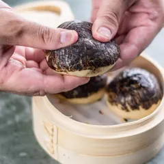 Our iconic Char Siu Pork Baos from the 'Moon House' menu, served in a traditional bamboo steamer. The unique marbled appearance hints at the rich flavor within.