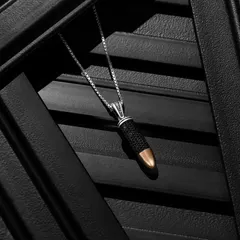 A moody close-up of a bullet-shaped pendant from Orionz Jewels. The dark, textured background and directional lighting create a sense of drama and highlight the unique design of the piece.