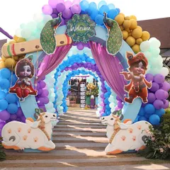A spectacular balloon tunnel entrance for a Krishna-themed welcome party. The arch is decorated with peacock and flute props, while cow cutouts stand guard, creating a playful and vibrant welcome for guests.