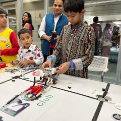 Students dressed in traditional attire for a festive event, working on their robots with family members looking on. We encourage a supportive community where learning and celebration go hand in hand.
