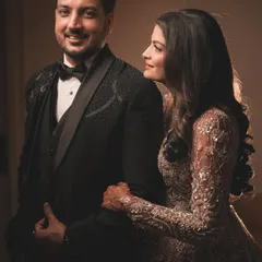 A classic and sophisticated portrait. The groom's sharp tuxedo and the bride's sparkling gown are captured with soft lighting that highlights their elegance and the loving glance they share.