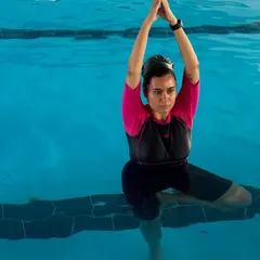 A participant practices a seated overhead stretch in the pool. The water provides gentle resistance, which helps to build strength while stretching.