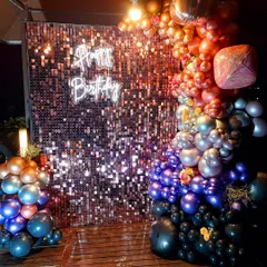 This vibrant birthday setup features a multi-colored chrome balloon garland cascading down a dark, shimmering sequin wall. The "Happy Birthday" neon sign stands out beautifully, creating a dramatic and festive atmosphere perfect for evening parties.
