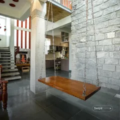 The indoor swing is a favorite feature in many homes I design. Here, it is suspended between a concrete pillar and a rugged stone wall, creating a perfect spot to relax and enjoy the view of the open-plan interior and puja area.