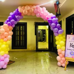 A colorful balloon archway to welcome guests to a birthday celebration, using a bright palette of purple, pink, orange, and yellow.