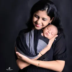 A mother's gentle smile radiates love as she cradles her sleeping newborn. This classic portrait uses a dark background to draw all attention to the peaceful and loving bond between mother and child.
