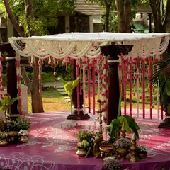A closer look at the outdoor wedding mandap. The structure is built with traditional dark wood pillars, and the roof is a delicate net of jasmine flowers, from which hang beautiful strings of pink carnations and lotus buds.