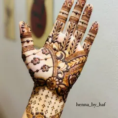 An intricate bridal henna design with a mix of floral and paisley elements. The palm features a large, detailed motif with hanging flowers, while the fingers are covered in leafy vines.