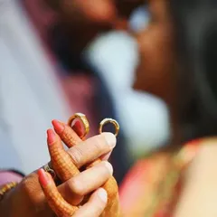 A close-up shot focusing on the couple's hands and their wedding rings, with the couple blurred romantically in the background.
