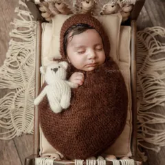 An overhead view of the rustic wooden bed setup, showing the baby cuddling a small teddy bear. We use soft, cozy props to keep your baby comfortable.