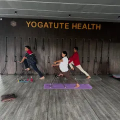 Students using chairs to support a lunge variation. The chair helps maintain balance and allows for a deeper stretch in the hip flexors and quadriceps without straining the knee.