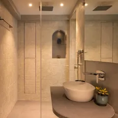 This master bathroom design features warm, textured tiles and a sleek, curved countertop with a vessel sink. We included hidden storage cabinets that are flush with the wall and an arched niche in the shower for toiletries.
