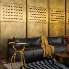 The lounge area of a private residence, where the back wall is clad in panels of burnished brass. The warm, metallic glow contrasts with the plush black leather sofa, creating a space that is grand yet cozy, minimal yet elegant.