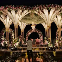 This magnificent reception stage combines art-deco inspired arches with lush floral arrangements and a reflective floor. The design creates an illusion of grandeur and depth, perfect for a glamorous evening event.