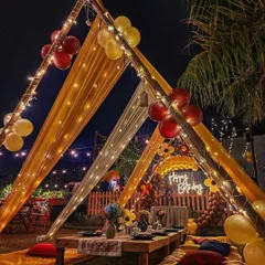 The main dining canopy, with a low wooden table set for dinner, surrounded by colorful cushions on the grass for a comfortable, bohemian-style party.