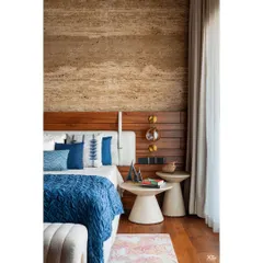 The bedroom in this luxury villa features a stunning travertine wall that adds natural texture and depth. Paired with warm wooden flooring and soft textiles, the space feels serene, inviting, and filled with sunlight.