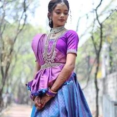 A full-length outdoor portrait of the bride in a beautiful blue and purple traditional half saree. The natural light and green background make the colors of her outfit pop.