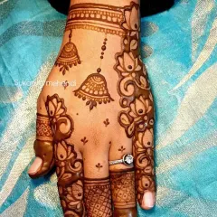 A delicate and stylish design perfect for Karvachauth. This Arabic-style mehendi features hanging jhumkas and lotus vines on the back of the hand.