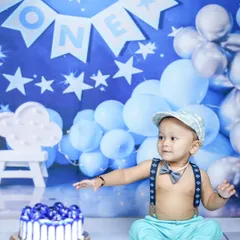 Ready for the cake! This is the moment just before the messy fun begins in a cake smash session. The setup is complete with a matching blue cake and a cute outfit.