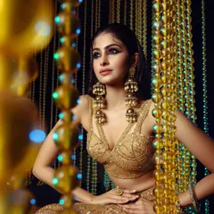 A striking shot of Manasa Varanasi for GNG Magazine, styled in a golden lehenga with dramatic, oversized jhumkas. The composition uses a beaded curtain to frame the subject, creating a rich, textured, and opulent portrait.