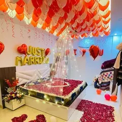 An elaborate romantic room setup featuring a bed covered in rose petals and a ceiling full of balloons. This decoration is perfect for a "Just Married" surprise or a special anniversary celebration.