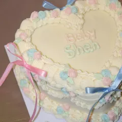 A sweet heart-shaped cake for a baby shower, decorated in a classic vintage style. We used pastel pink and blue buttercream rosettes and delicate ribbons to create this adorable centerpiece.