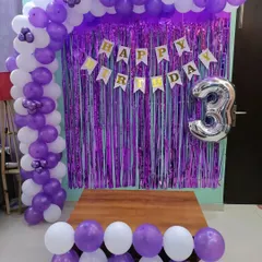 A simple and pretty half-arch in purple and white for a 3rd birthday. The setup includes a shimmer curtain, banner, and number balloon.