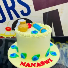 A custom cake celebrating Janmashtami, themed around Lord Krishna. This design includes a fondant flute, a pot of butter, and peacock feathers.