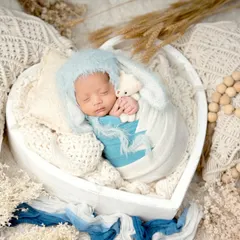 A wide shot showing a complete newborn setup. The baby is sleeping peacefully in a heart-shaped basket, surrounded by soft fabrics, wooden beads, and dried botanicals for a rustic and gentle feel.
