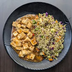 A top-down view of the tofu and pesto brown rice dish, showing the generous portion of protein and the colorful mix of vegetables in the rice.