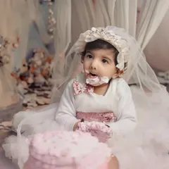 A sweet and gentle cake smash for a little princess. Dressed in a beautiful white gown and bonnet, she delicately explores her very first birthday cake in a dreamy, floral setting.