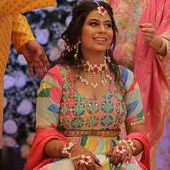 A beautiful Haldi bride seated for her ceremony. Her makeup is bright and cheerful, matching her colorful outfit and floral jewelry.
