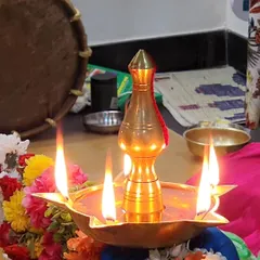 A close-up of a traditional brass lamp, lit for a pooja. The lamp itself is an object of worship, symbolizing the divine light.