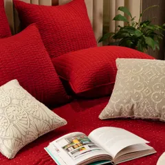 A cozy bedroom scene featuring a bed dressed in rich red linens and assorted textured pillows. An open book invites the viewer to imagine relaxing in this comfortable and stylish space.