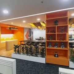 This view shows the transition from the workspace to the canteen, with a decorative shelving unit acting as a subtle divider. The high-top table and stools offer a casual spot for employees to eat or work.