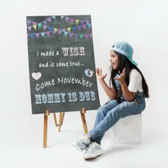 A creative pregnancy announcement photo where a proud big sister-to-be sits next to a chalkboard that reads "I made a wish and it came true... Come November Mommy is due".