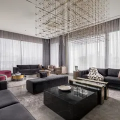 This angle showcases the thoughtful layout of the entertainment lounge, designed for easy conversation. The arrangement includes multiple custom sofas and ottomans in grey velvet, a black marble coffee table, and a large, contemporary chandelier that defines the seating area.