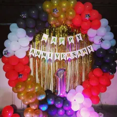 A first-anniversary celebration with a full balloon ring in red, black, white, and gold, set against a gold shimmer curtain.