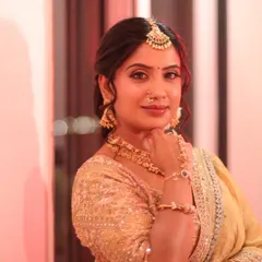 A warm, indoor shot that highlights the bride's radiant glow. The makeup is soft and luminous, complementing the gold tones of her outfit and jewellery.
