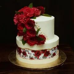 This two-tier wedding cake features a cascade of fresh red roses and carnations. The bottom tier is wrapped in an edible print with a matching rose pattern, adding a unique and personal touch.