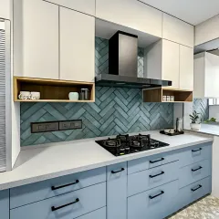 This kitchen features a lovely two-tone color scheme with pastel blue base cabinets and off-white uppers. The herringbone-patterned teal backsplash adds a unique texture and focal point, while the open wood shelves provide a warm contrast.