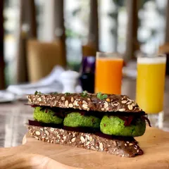 A healthy falafel sandwich in a multigrain bread. The shot is taken on a rustic wooden board, giving it a wholesome, organic feel perfect for a health-conscious cafe.