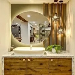 This washbasin area features a large, round backlit mirror that creates a beautiful focal point. The wooden vanity and hanging pendant lights add warmth and a touch of industrial chic.
