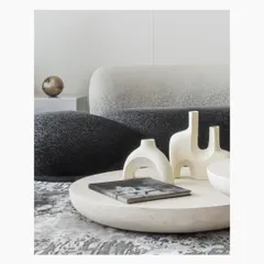 A close-up of the circular stone coffee table, adorned with minimalist white ceramic sculptures. The textures of the boucle sofa and the abstract grey rug create a rich, tactile experience, showcasing our love for layering materials.