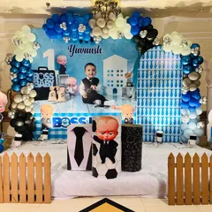 A full stage setup for a classic Boss Baby first birthday party. I used a custom-printed backdrop with the child's name, multiple character cutouts, a themed balloon arch in blue, black, and silver, and a small picket fence to complete the look.