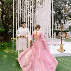 The bride twirls in her beautiful pink lehenga as she approaches her groom, who waits for her amidst a curtain of white flowers. A moment of joyful anticipation.