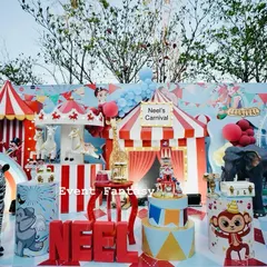 A bright and colorful carnival setup for Neel's birthday. The stage is packed with fun elements like a circus tent, carousel horses, a Ferris wheel, and animal props, ready for a day of fun.