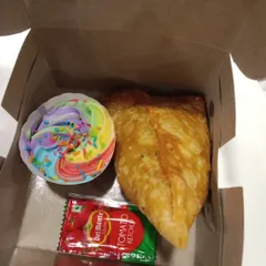 A snack box prepared for an event, featuring one of our rainbow cupcakes alongside a savory samosa and ketchup. A perfect balance of sweet and savory.