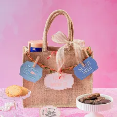 This Mom's Jute Bag Gift Hamper combines rustic charm with sweet treats. It's filled with cookies and bliss bars and decorated with cute tags like 'Super Mom' and 'Home is where Mom is'.
