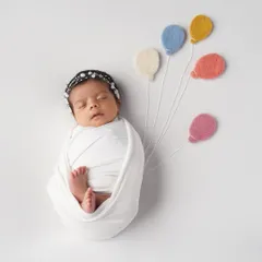 So simple, yet so sweet. This little one is wrapped snugly and holding onto tiny felt balloons, creating a whimsical and adorable image.